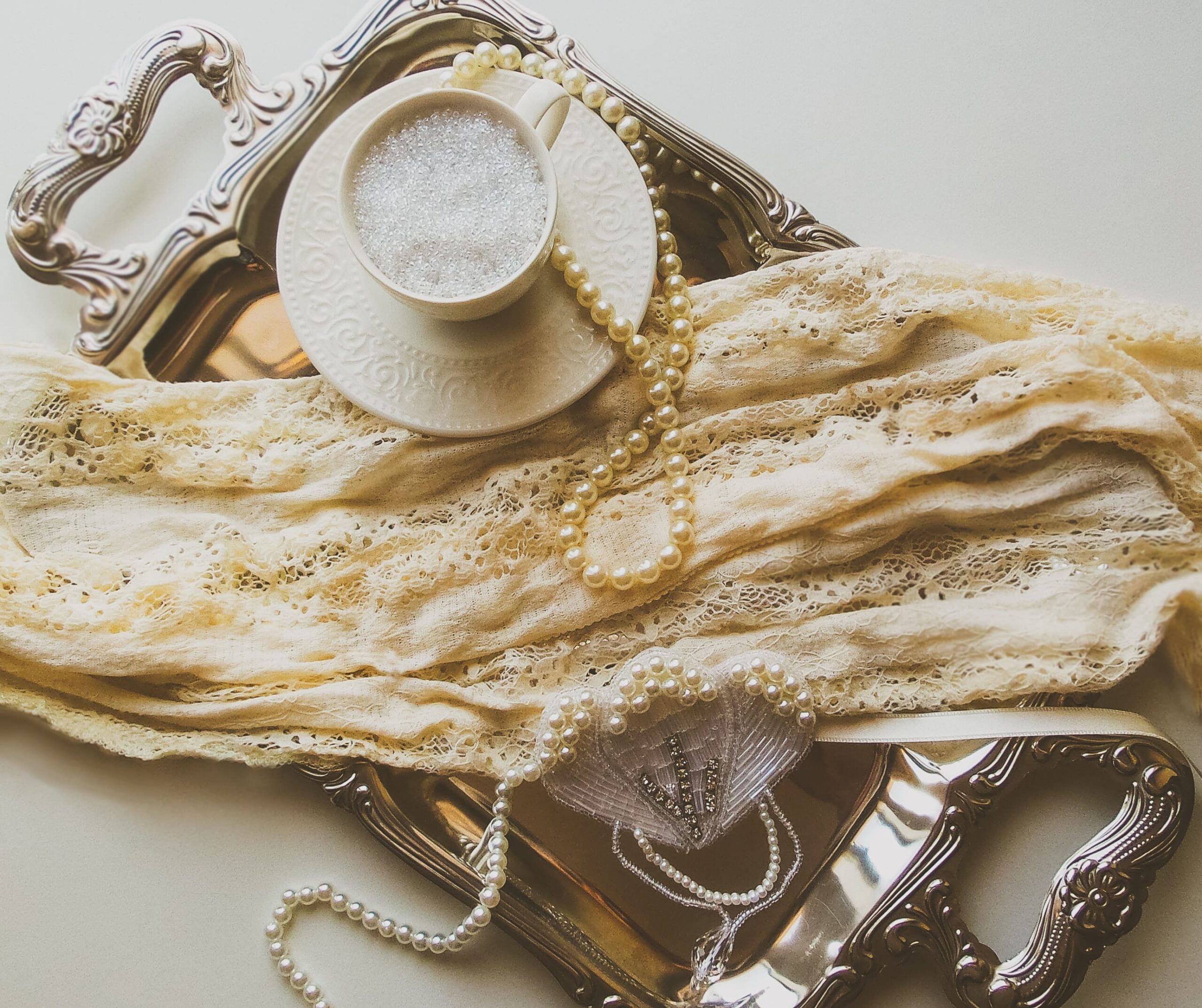 romantic academia flat lay of a coffee, pearls, and a lace clothing piece on a tray